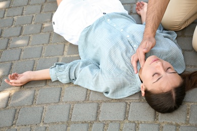 Photo of Young man checking pulse of unconscious woman outdoors. First aid