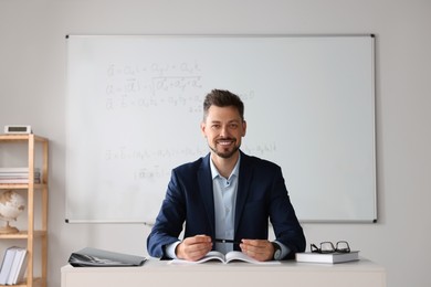 Photo of Happy teacher sitting at table in classroom