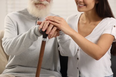 Senior man with walking cane and young woman indoors, closeup