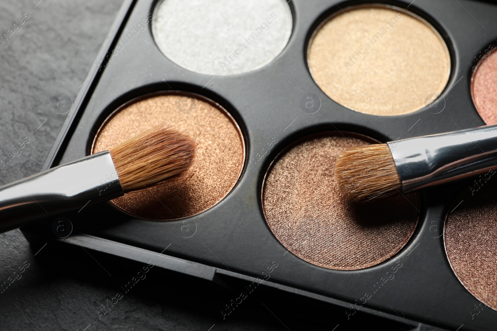 Photo of Beautiful eye shadow palette with brushes on dark grey textured table, closeup