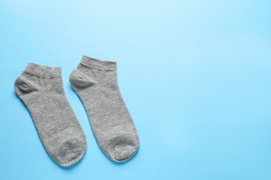 Pair of grey socks on light blue background, flat lay. Space for text