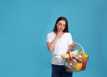 Young woman with shopping basket full of products on blue background