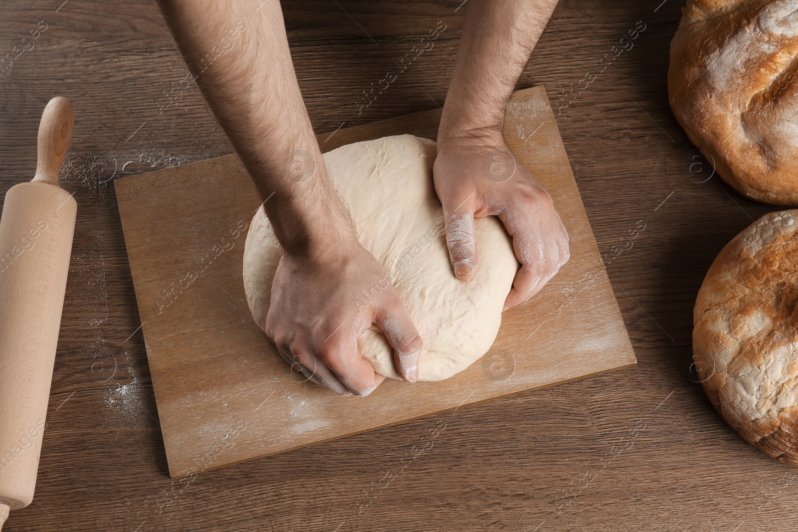 Photo of Male baker preparing bread dough at wooden table, above view