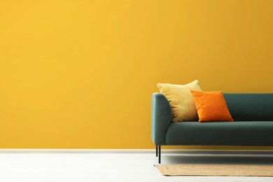 Stylish sofa with cushions and rug near orange wall indoors, space for text. Interior design