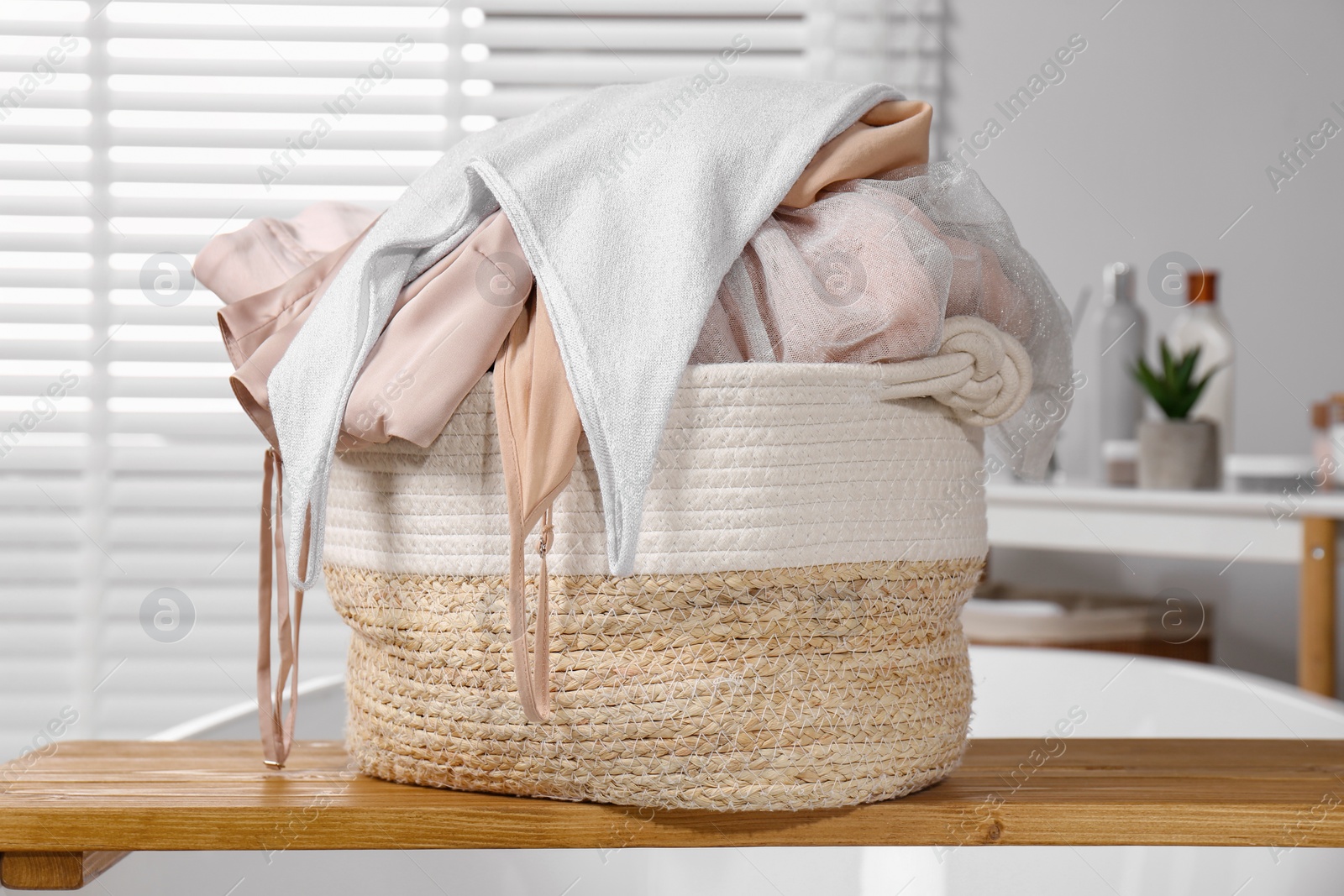 Photo of Wicker laundry basket with clothes on wooden tray in bathroom