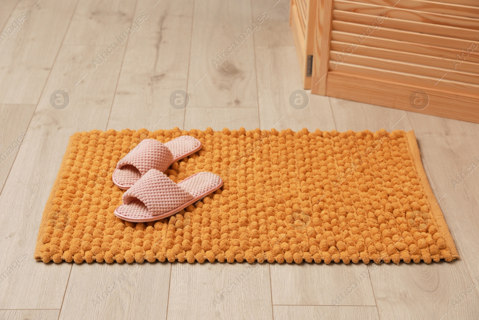 Photo of New yellow bath mat with soft slippers on floor indoors