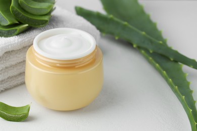 Jar with cream, cut aloe leaves and towel on white table, closeup