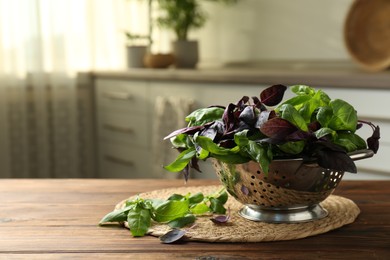 Photo of Metal colander with different fresh basil leaves on wooden table in kitchen. Space for text