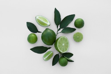 Whole and cut fresh limes with leaves on white background, flat lay