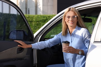 Photo of Coffee to go. Happy woman with paper cup of drink in car outdoors