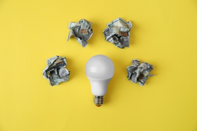 Photo of Flat lay composition with lamp bulb and crumpled money on color background