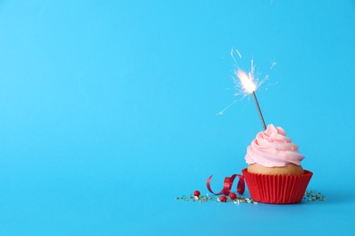 Photo of Birthday cupcake with burning sparkler on light blue background. Space for text