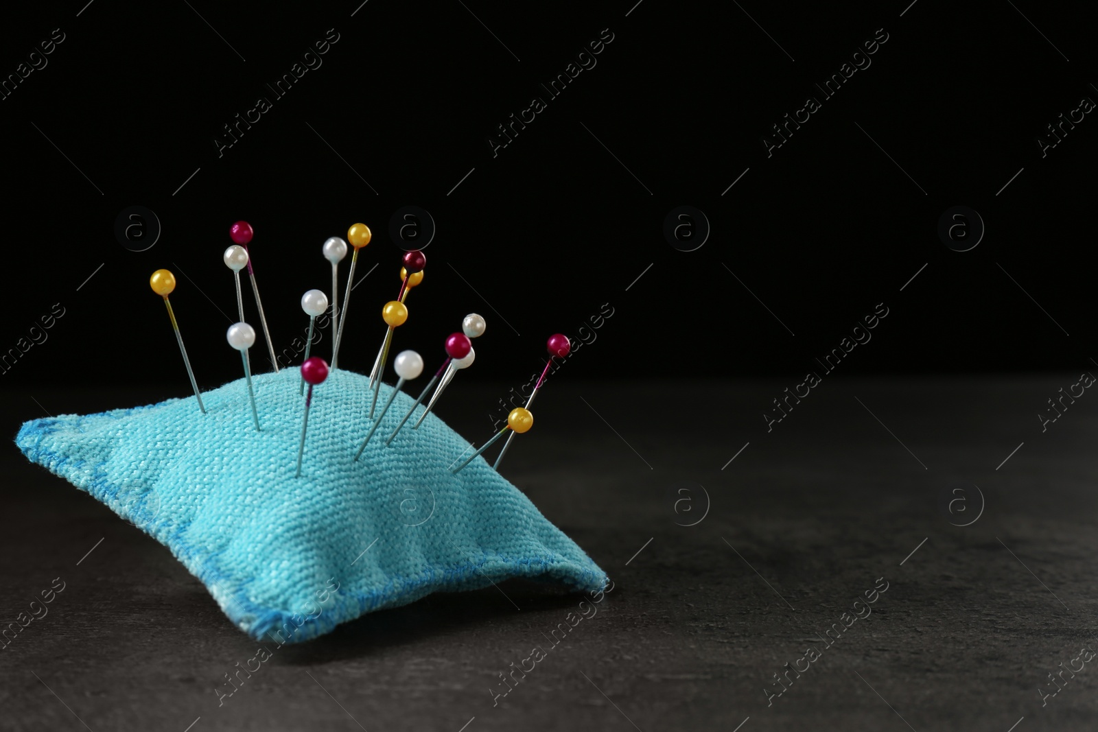 Photo of Light blue cushion with pins on grey stone table. Space for text