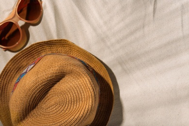 Hat and sunglasses on beach sand, top view. Space for text