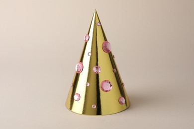 Photo of One shiny golden party hat with rhinestones on beige background