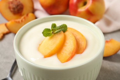 Photo of Delicious yogurt with fresh peach and mint in bowl on table, closeup