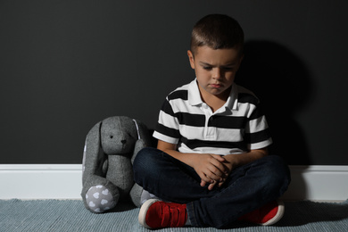 Photo of Sad little boy with toy near black wall. Domestic violence concept