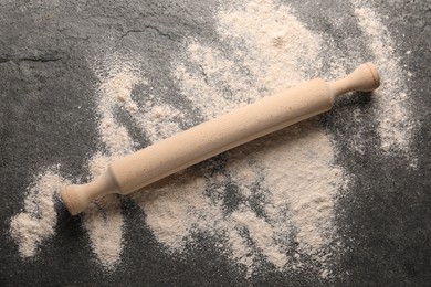 Photo of Scattered flour and rolling pin on grey textured table, top view