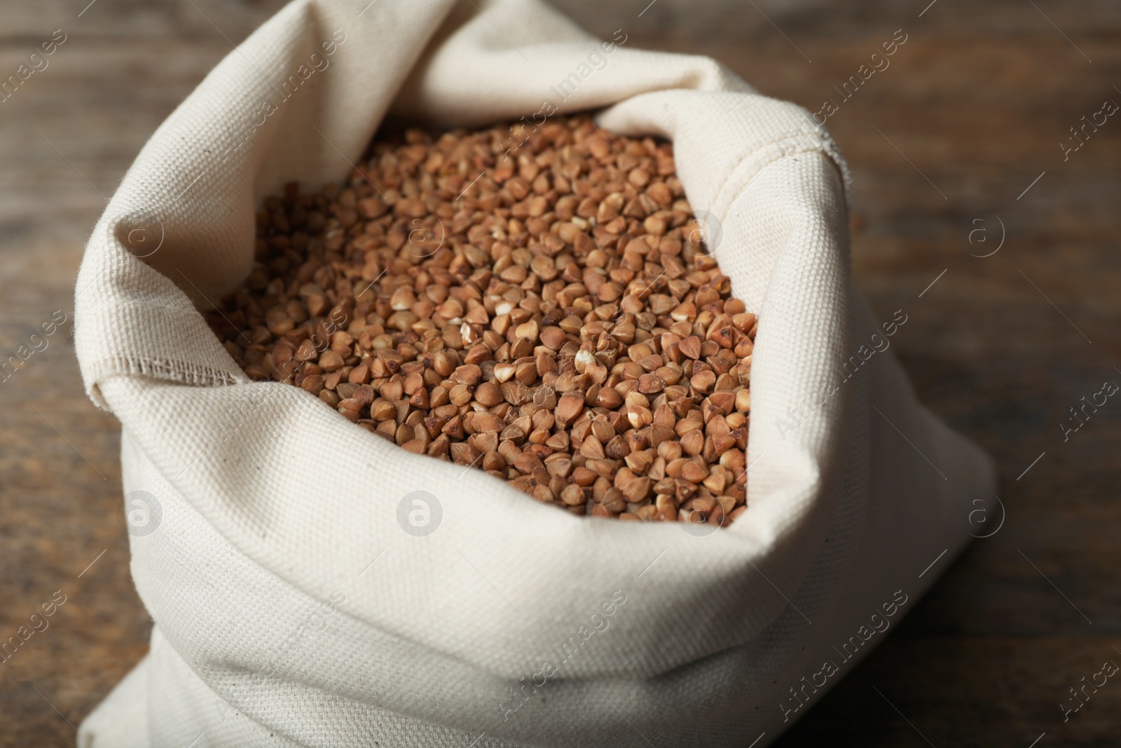 Photo of Uncooked buckwheat in sackcloth bag on wooden table