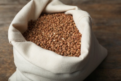 Photo of Uncooked buckwheat in sackcloth bag on wooden table