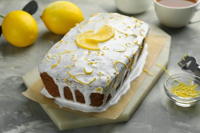 Photo of Tasty lemon cake with glaze, citrus fruits and zest on gray textured table, closeup