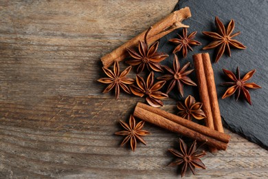Photo of Aromatic cinnamon sticks and anise stars on wooden table, flat lay. Space for text
