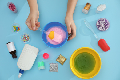 Little girl making slime toy on light blue background, top view