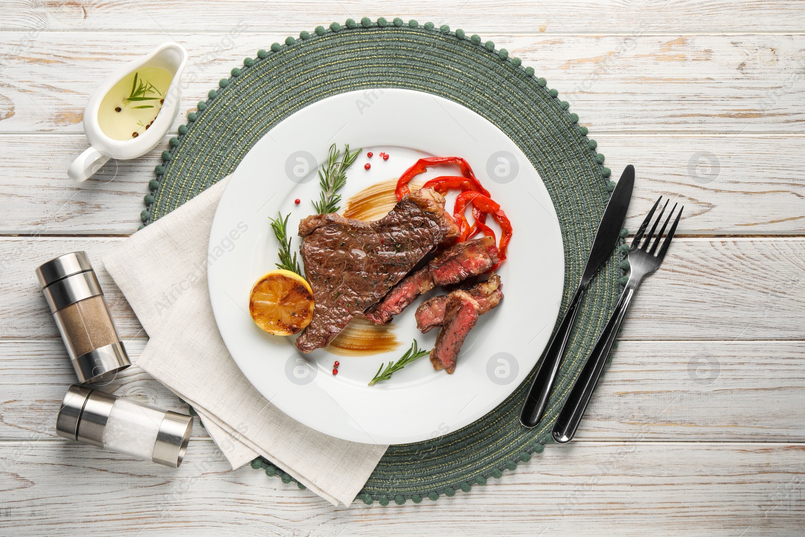 Photo of Delicious grilled beef steak with pepper and spices served on light wooden table, flat lay