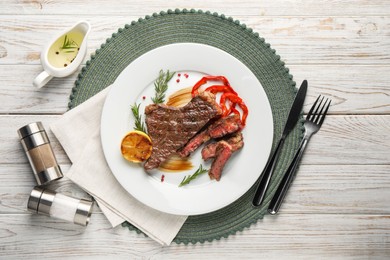 Photo of Delicious grilled beef steak with pepper and spices served on light wooden table, flat lay