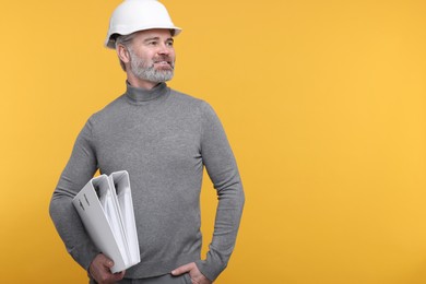 Photo of Architect in hard hat holding folders on orange background. Space for text