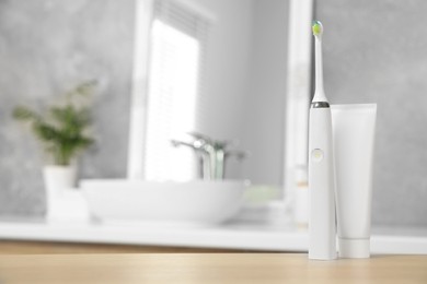 Photo of Electric toothbrush and tube with paste on wooden table in bathroom. Space for text