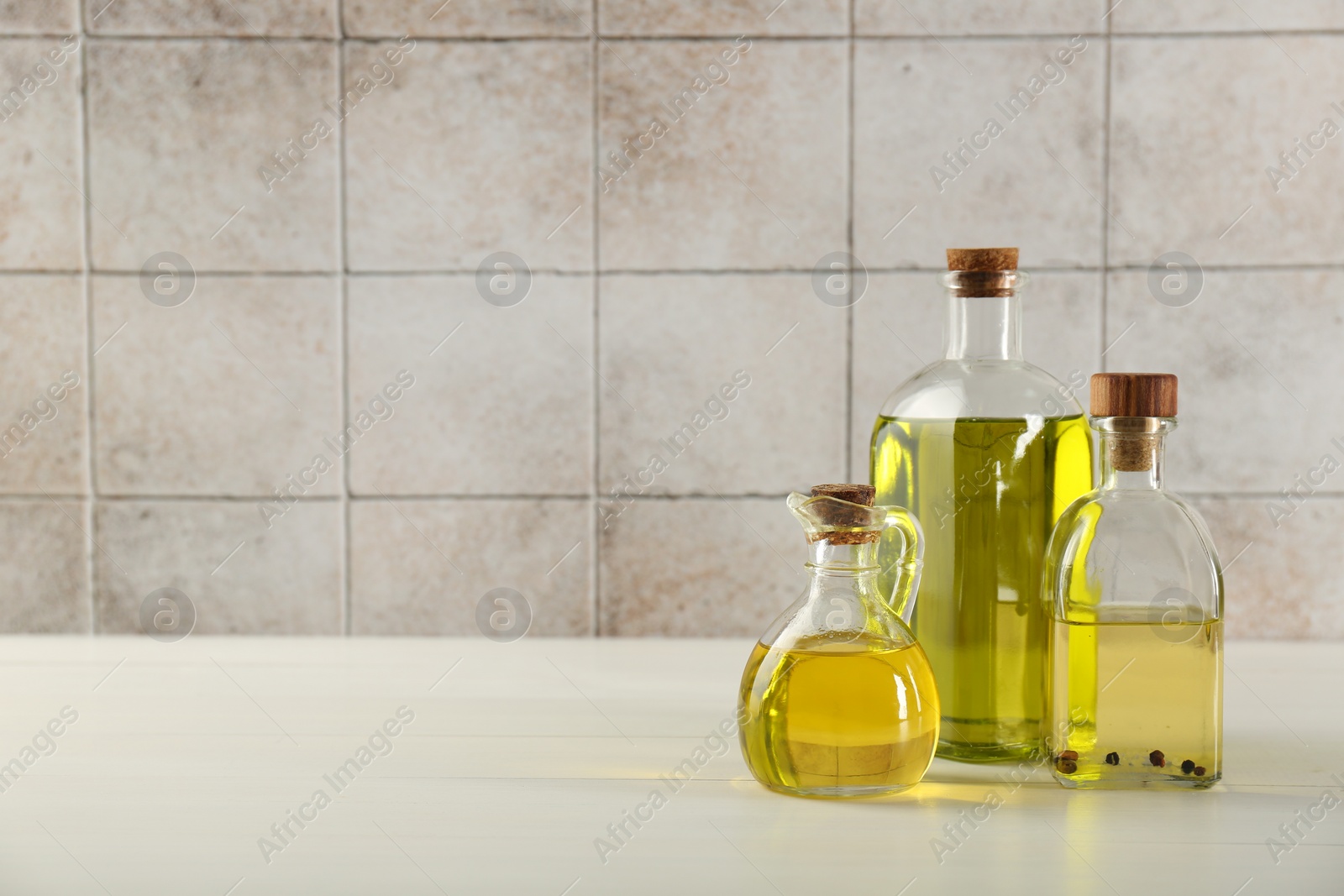 Photo of Vegetable fats. Different oils in glass bottles on white wooden table against tiled wall, space for text