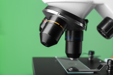 Modern medical microscope with glass slide on green background, closeup