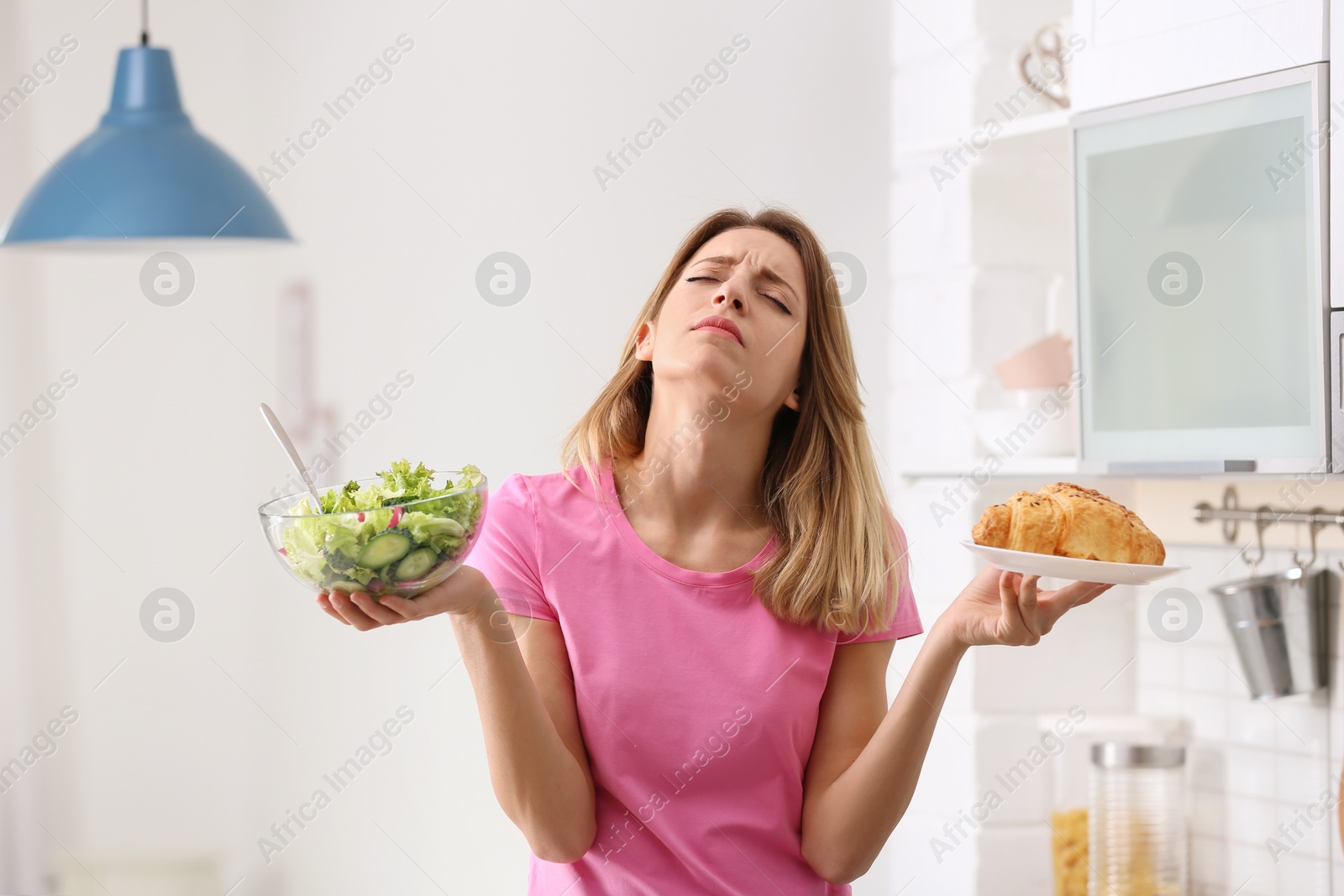 Photo of Woman choosing between vegetable salad and dessert in kitchen. Healthy diet