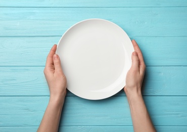 Woman with empty plate at wooden table, top view