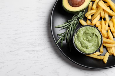 Photo of Plate with french fries, guacamole dip, rosemary and avocado served on white wooden table, top view. Space for text