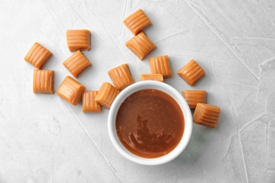 Delicious caramel candies and sauce on light background