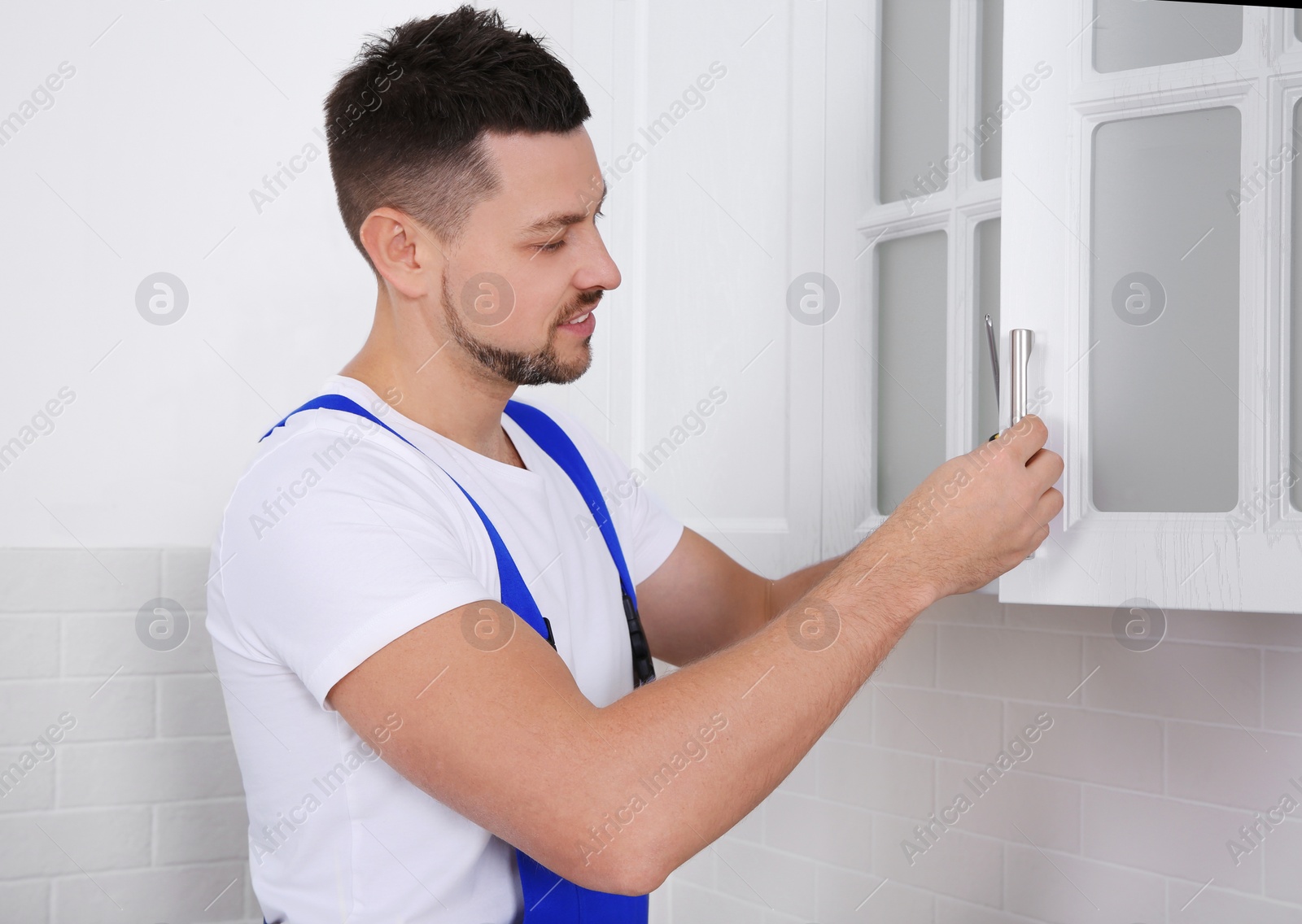 Photo of Worker installing handle of cabinet door with screwdriver in kitchen