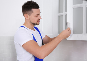 Worker installing handle of cabinet door with screwdriver in kitchen