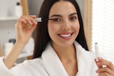 Photo of Beautiful woman applying serum onto her eyelashes in bathroom. Cosmetic product