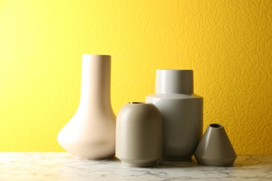 Photo of Stylish ceramic vases on white marble table against yellow background