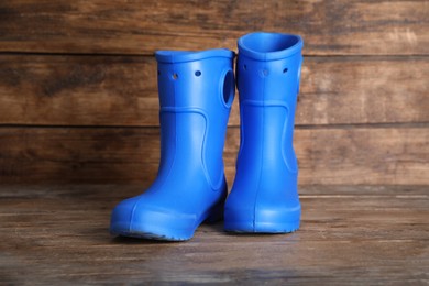 Photo of Bright blue rubber boots on wooden surface