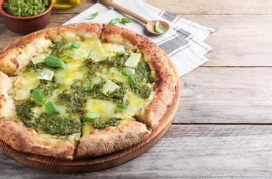 Photo of Delicious pizza with pesto, cheese and basil on wooden table. Space for text