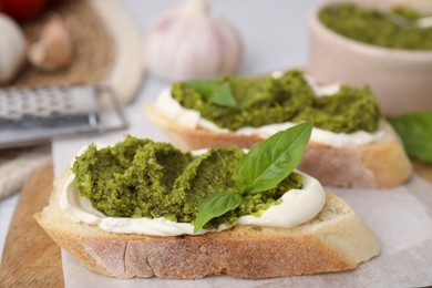 Tasty bruschettas with cream cheese, pesto sauce and fresh basil on wooden board, closeup