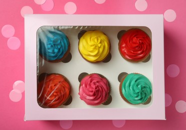 Box with different cupcakes and confetti on pink background, flat lay