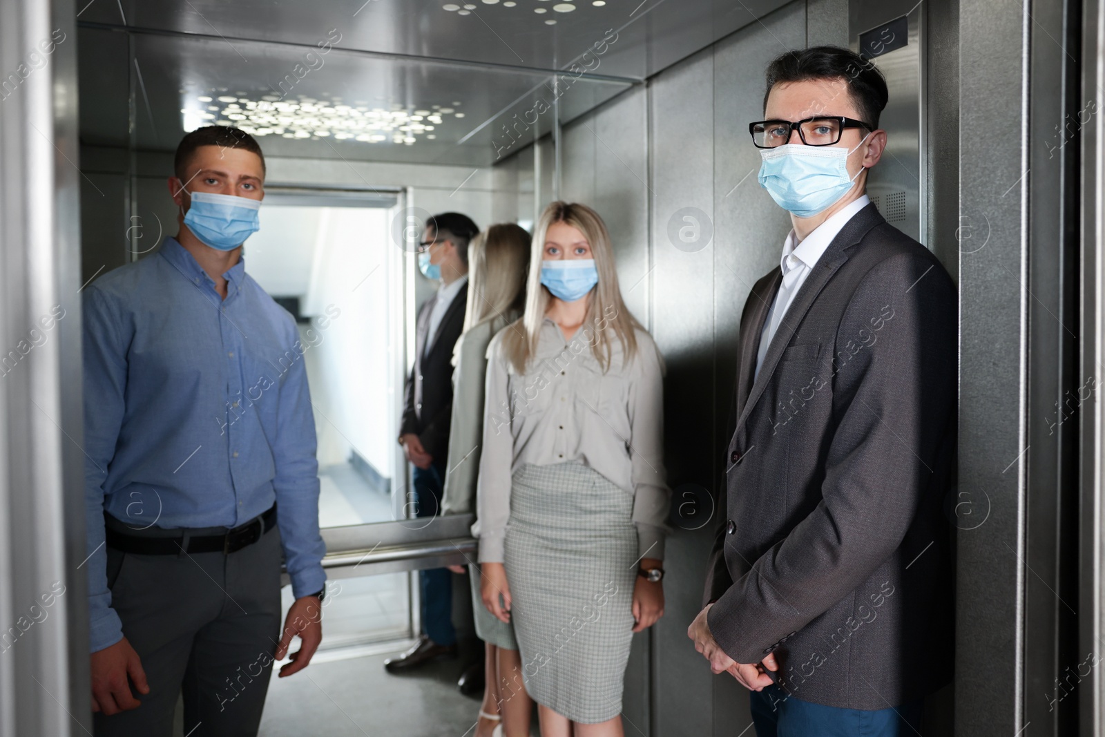 Photo of Group of people with face masks in elevator. Protective measure