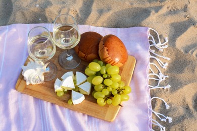 Glasses with white wine and snacks for beach picnic on sand outdoors, above view