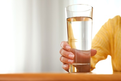 Woman holding glass of water at wooden table, closeup with space for text. Refreshing drink