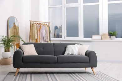 Photo of Stylish living room interior with comfortable grey sofa and clothing rack