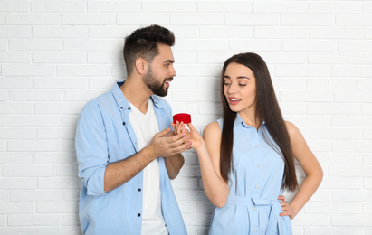 Photo of Young woman with engagement ring making marriage proposal to her boyfriend near white brick wall